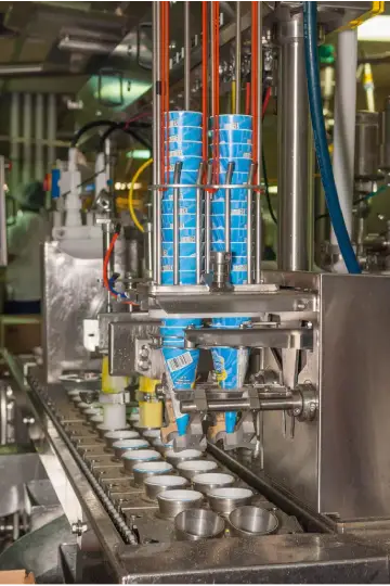 Automated industrial machinery filling blue cups with a food product on a conveyor belt