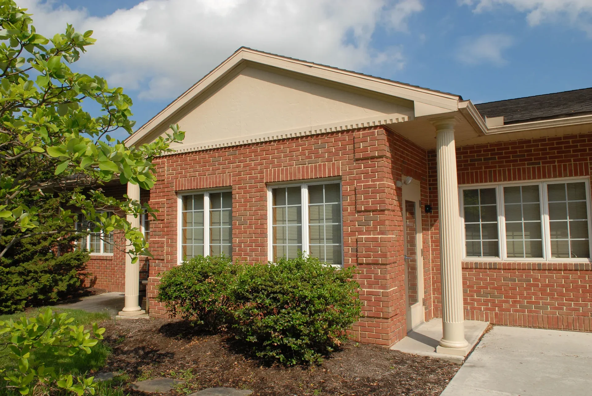A single-story brick building with white columns and green shrubbery under a clear sky