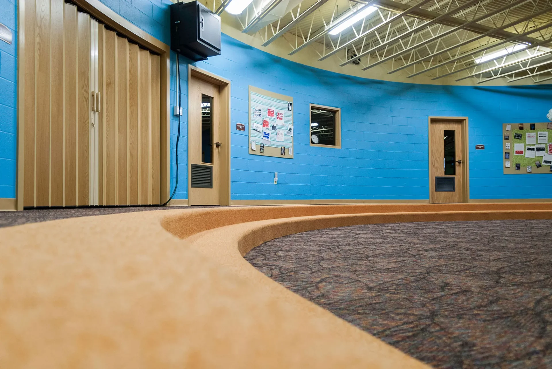 Interior of a room with blue walls, wooden doors, a bulletin board, and carpeted floors