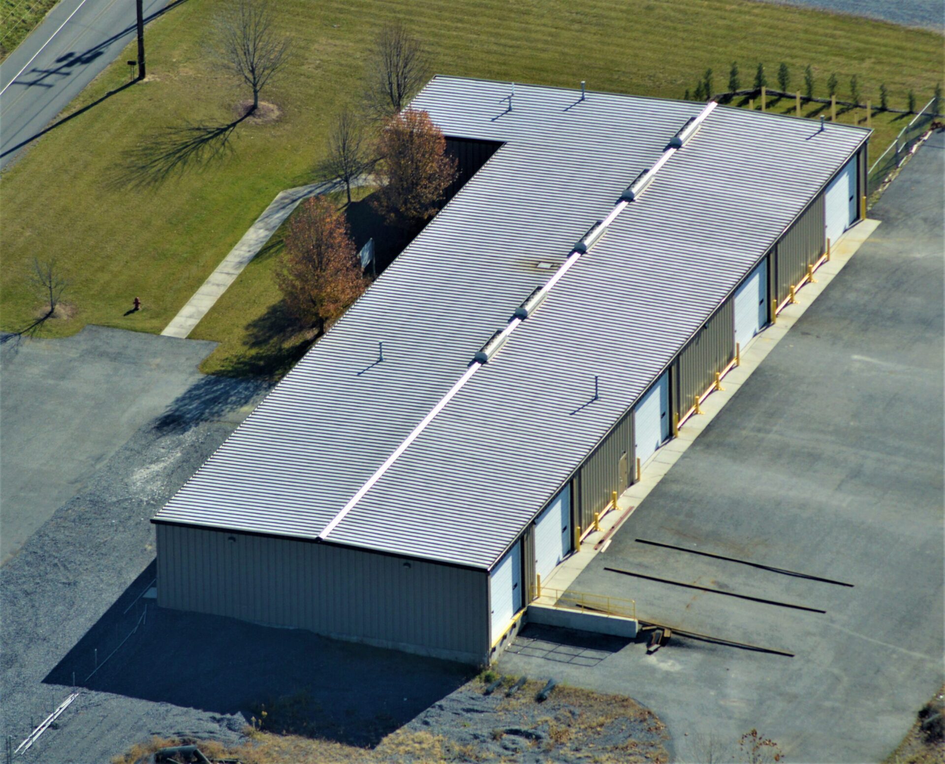 Aerial view of a long industrial building with a striped roof and adjacent parking area