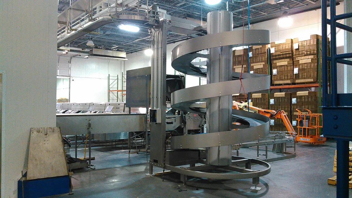Industrial spiral conveyor in a warehouse with boxes and machinery in the background Industrial spiral conveyor in a warehouse with boxes and machinery in the background