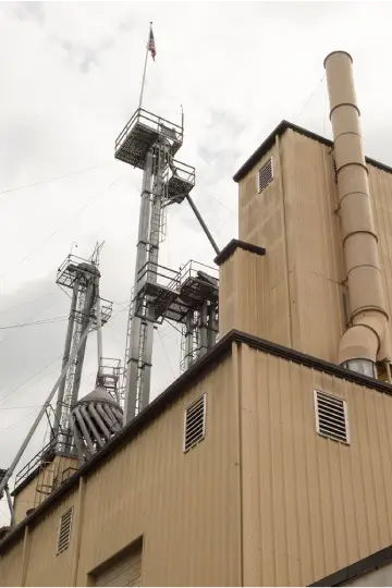 Industrial tower with stairs, railings, and American flag, attached to a beige building with vents