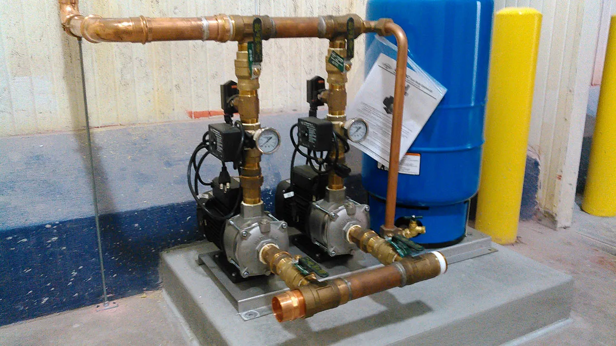 Industrial water pumps connected to copper piping with gauges near a blue drum and yellow bollards. Industrial water pumps connected to copper piping with gauges near a blue drum and yellow bollards