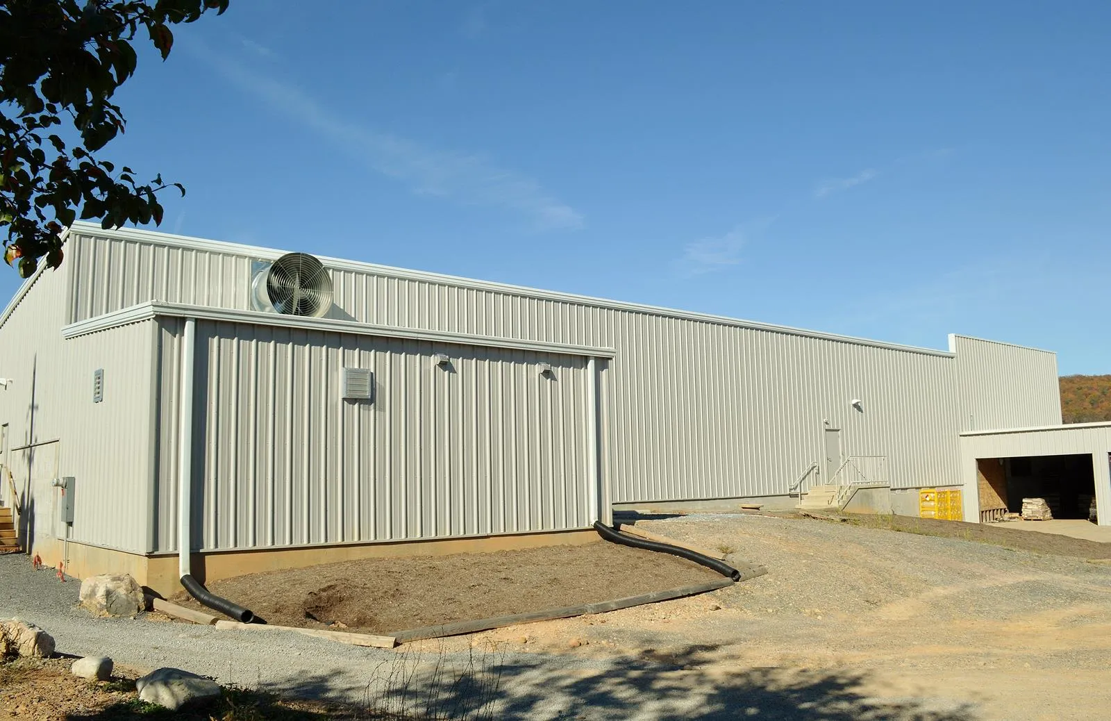 Large industrial metal building with external exhaust fan and clear blue sky