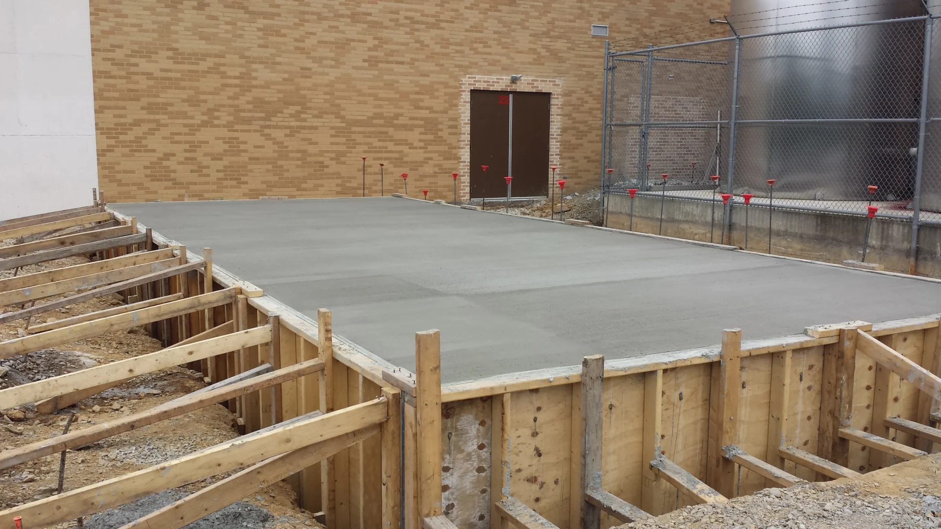 Freshly poured concrete slab with wooden formwork against a brick building