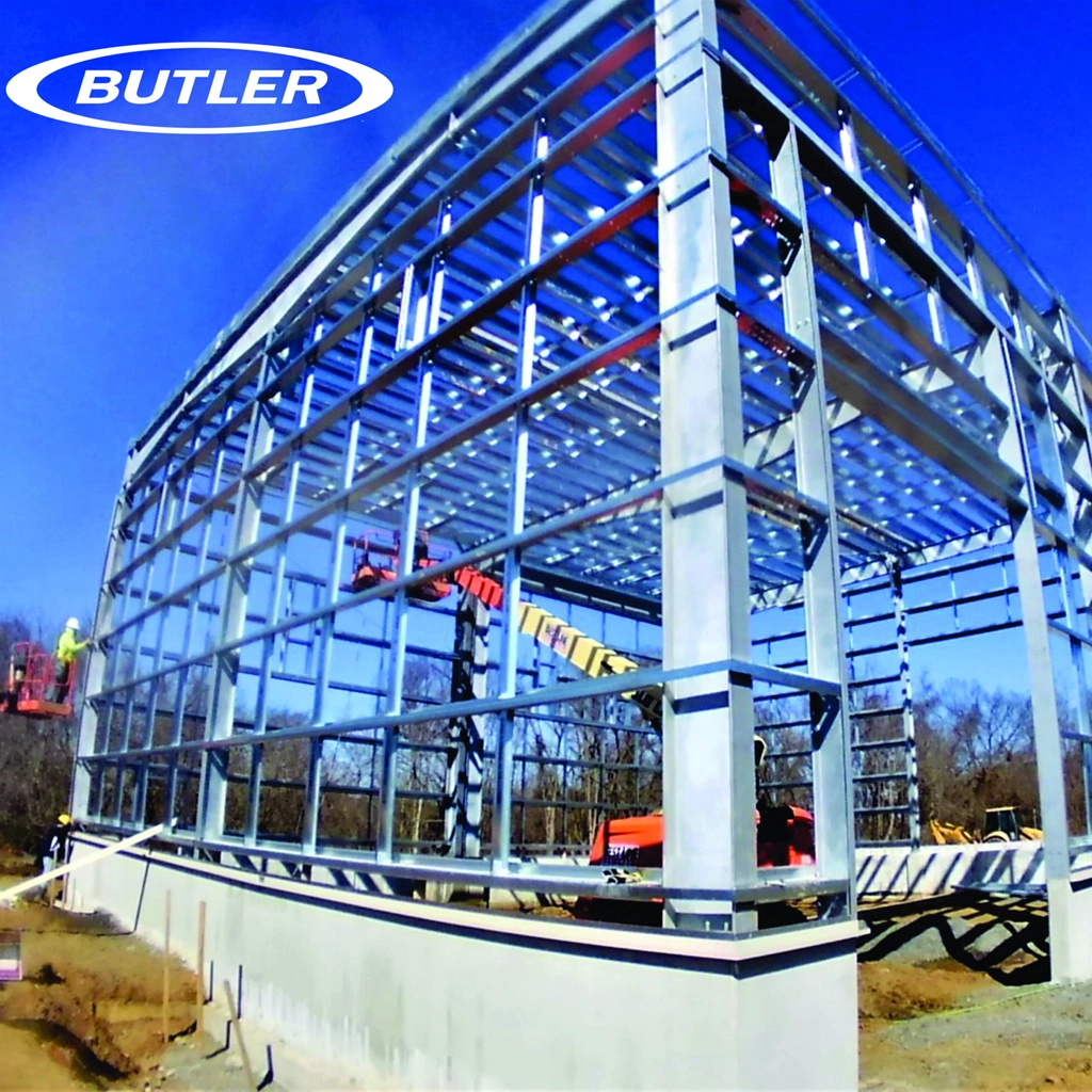 A metal building frame under construction with a bright blue sky overhead, featuring workers and machinery on site