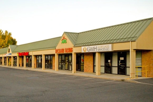 Castle-Commons-thumb Exterior view of a strip mall featuring various shops, including a mortgage service, with a green metal roof and brick facade